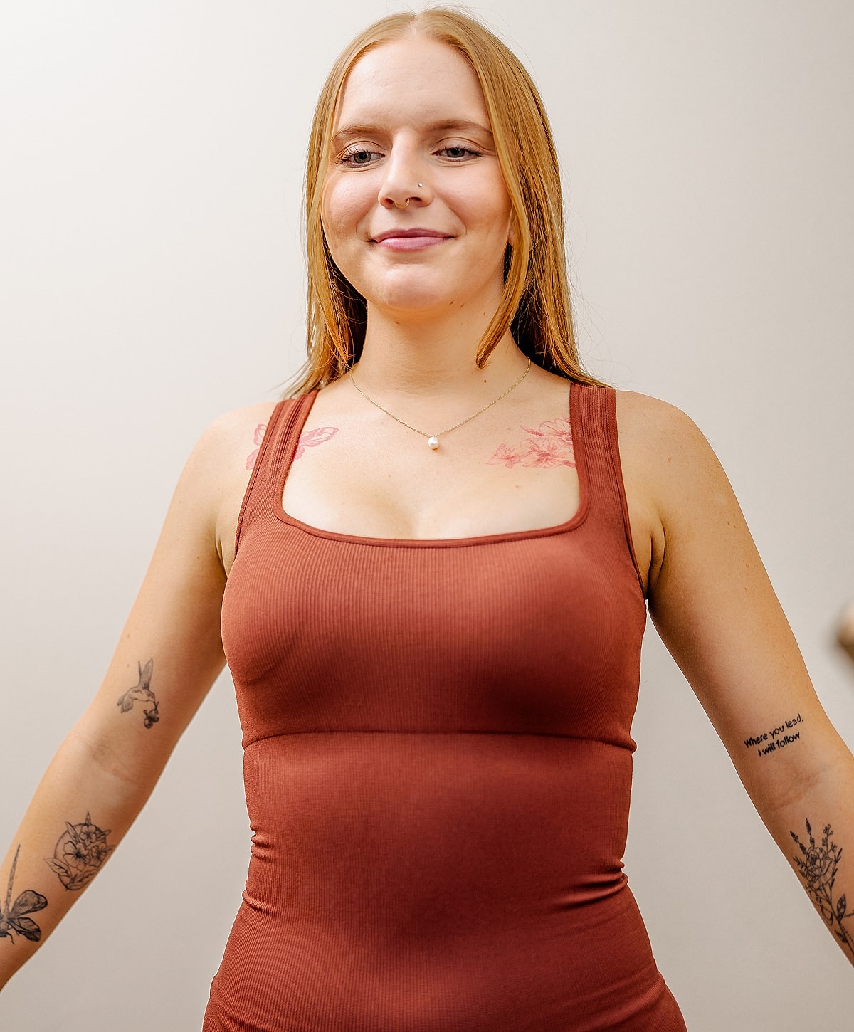 Woman in brown top with tattoos, smiling.